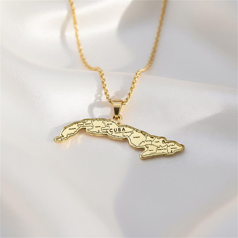 A gold-colored pendant necklace with a map of Cuba on it, resting on a white fabric background.