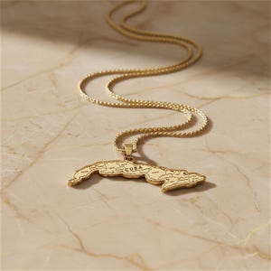 A gold-colored pendant necklace with a map of Cuba on it, resting on a marble surface.