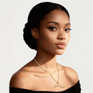 A woman with dark hair wearing a black off-the-shoulder top and a gold necklace with a pendant.