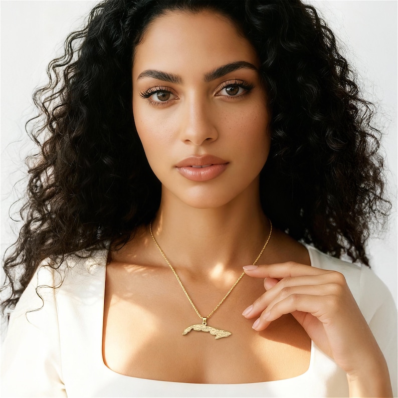 A woman with curly dark hair wearing a white top and a gold necklace with a pendant.
