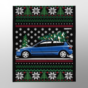 Op de afbeelding: Zwarte deken met een blauwe auto die een kerstboom op het dak vervoert. De deken heeft een feestelijk patroon met sneeuwvlokken, kerstbomen en rode en groene accenten. De tekst "TUNERHYPE" is zichtbaar.