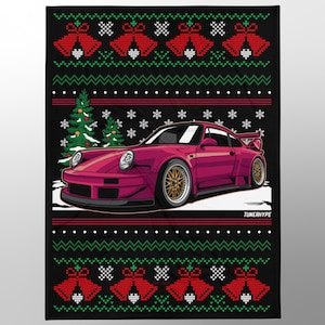 Op de afbeelding: Zwarte deken met een kersttrui-ontwerp. Het ontwerp toont een magenta sportwagen, kerstbomen, sneeuwvlokken en rode bellen. De tekst "TUNERHYPE" staat onderaan de deken.