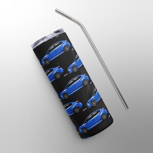 May include: A stainless steel tumbler with a black background featuring a pattern of blue cars. A silver-colored, curved metal straw is positioned next to the tumbler. The tumbler has a silver lid.