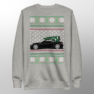 May include: A gray sweatshirt with a festive Christmas design. The design features a black car with a Christmas tree on top, set against a pattern of snowflakes, Christmas trees, and geometric shapes in red, green, and white.