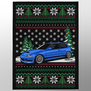 Op de afbeelding: Een zwarte deken met een blauwe autografiek, kerstbomen, sneeuwvlokken en een feestelijk truienpatroon. De auto is een felblauwe hatchback met zilveren velgen. De tekst "TUNERHYPE" is zichtbaar.