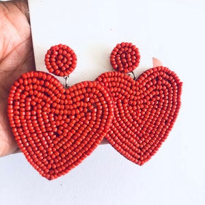 May include: A pair of red beaded heart-shaped earrings. The earrings are made of small, round beads that are strung together to create a heart shape. The earrings are approximately 5 cm long and have a silver hook fastening.