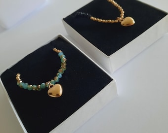 Puede incluir: Dos collares de corazón de oro con cadenas de cuentas. Un collar tiene cuentas verdes y el otro tiene cuentas doradas. Ambos collares están en cajas blancas con interiores de terciopelo negro.