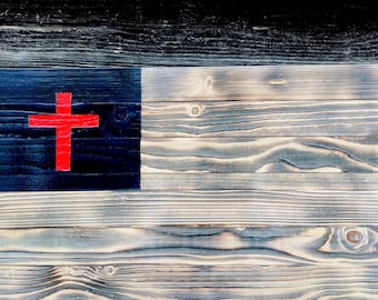 Könnte beinhalten: Ein Holzschild mit einer abgenutzten Oberfläche, das ein rotes Kreuz auf schwarzem Hintergrund zeigt. Das Schild besteht aus mehreren Holzbrettern, was ihm ein rustikales Aussehen verleiht.