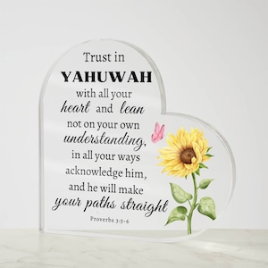 Puede incluir: Un letrero de acrílico transparente en forma de corazón con un diseño de girasol y mariposa. El letrero presenta el texto "Trust in YAHUWAH with all your heart and lean not on your own understanding, in all your ways acknowledge him, and he will make your paths straight" y la referencia bíblica "Proverbs 3:5-6".