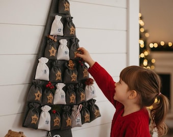May include: A gray felt Christmas tree advent calendar with numbered burlap sacks. A wooden star tops the tree. A child in a red sweater reaches for a star-shaped ornament. The calendar is mounted on a white wall.