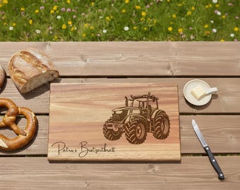 May include: A wooden cutting board with a tractor design and the text "Petra's Brotzeitbrett" is displayed on a wooden table. A loaf of bread, a pretzel, a small dish of butter, and a knife are also on the table.