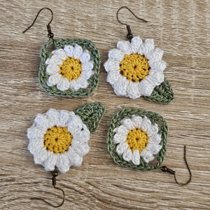 May include: Four crocheted daisy earrings with green leaves. The earrings are made with white and yellow yarn and have bronze hooks.