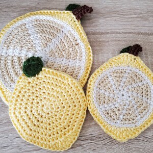 May include: Two crocheted lemon-shaped coasters. The larger coaster is white and yellow with a brown stem. The smaller coaster is yellow with a green stem.