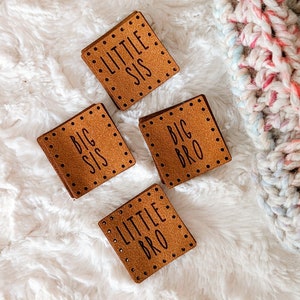 May include: Four brown leather patches with white stitching and black text. The patches read "Big Sis", "Little Sis", "Big Bro", and "Little Bro".