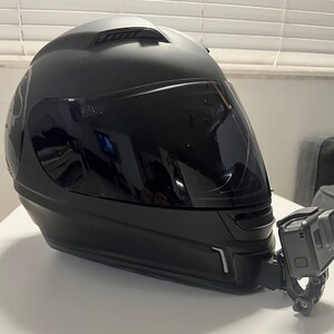 May include: A black motorcycle helmet with a clear visor and a GoPro camera mounted on the side.