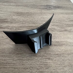 May include: Black plastic flash diffuser with a curved shape and a mounting bracket. The diffuser is designed to soften and spread light from a flash.