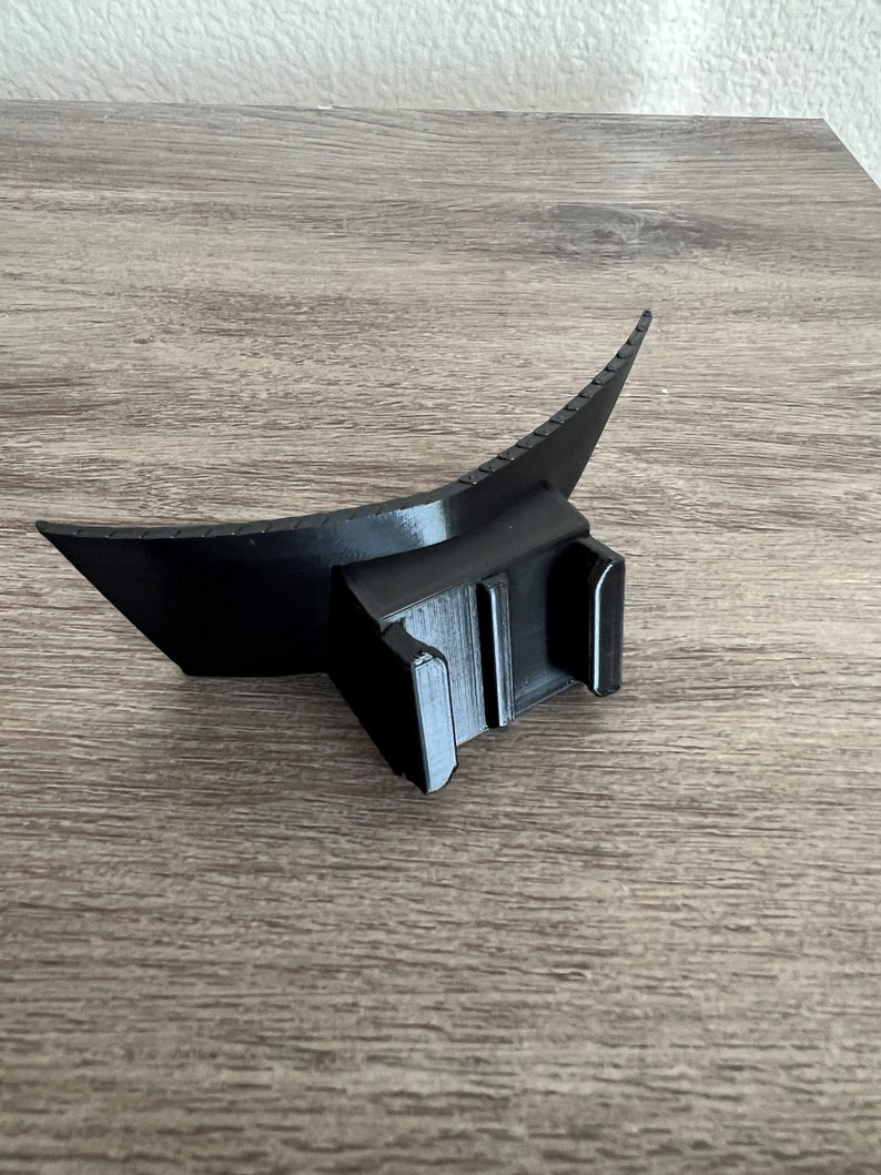 May include: Black plastic flash diffuser with a curved shape and a mounting bracket. The diffuser is designed to soften and spread light from a flash.