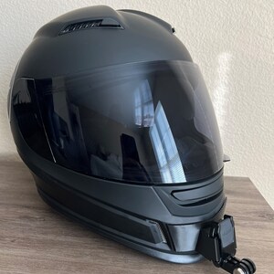 May include: A black motorcycle helmet with a clear visor and a GoPro camera mount attached to the side.