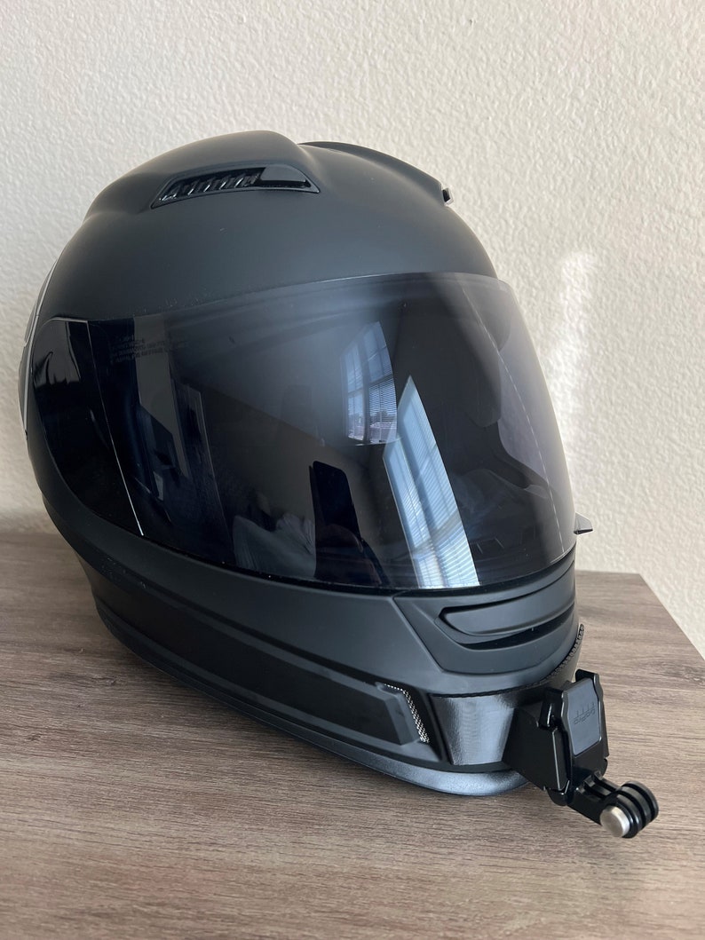 May include: A black motorcycle helmet with a clear visor and a GoPro camera mount attached to the side.