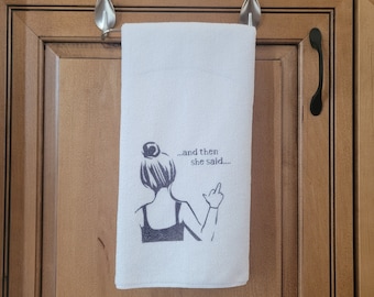 May include: White kitchen towel with a black and white illustration of a woman giving the middle finger with the text "...and then she said..."