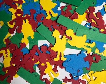 May include: A colorful assortment of paper cutouts in red, yellow, blue, and green. The shapes include stylized figures and rectangular tags, scattered across the surface. The figures appear to be cartoon characters.