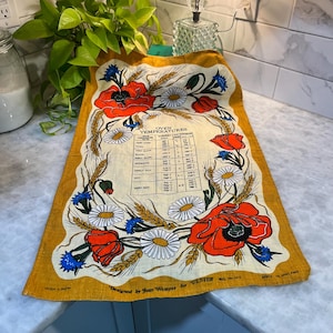 Könnte beinhalten: Ein Vintage-Küchentuch aus irischem Leinen mit einem senfgelben Rand. Das Tuch zeigt ein Blumendesign mit roten Mohnblumen, weißen Gänseblümchen, blauen Kornblumen und Weizenähren. Der Text enthält "Oven Temperatures" und "Designed by Joan Wemyss for Ulster."