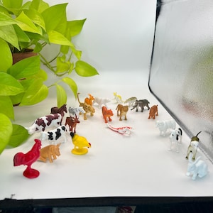 May include: A collection of small plastic animal figurines, including a red rooster, cows, tigers, and a zebra. The figurines are in various colors and poses, creating a miniature farm and zoo scene.
