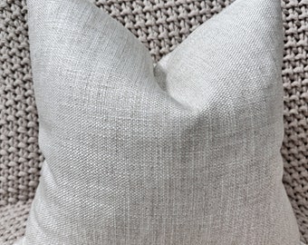 Peut inclure: Un coussin de canapé gris clair avec un tissu texturé. Le coussin est carré et a un design simple.