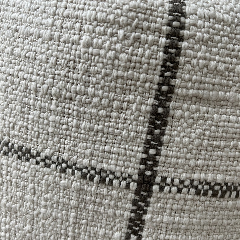 May include: Close-up of a woven fabric with a white background and black stripes. The fabric has a textured, rough surface.