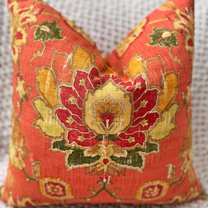 May include: A red pillow with a floral pattern in shades of yellow, orange, green, and red. The pattern is intricate and detailed, with a central flower surrounded by smaller flowers and leaves.