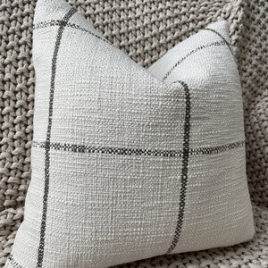 May include: A white throw pillow with a black and white plaid pattern. The pillow is made of a soft, textured fabric.