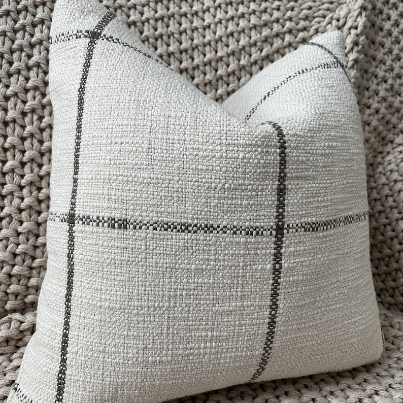 May include: A white throw pillow with a black and white plaid pattern. The pillow is made of a soft, textured fabric.