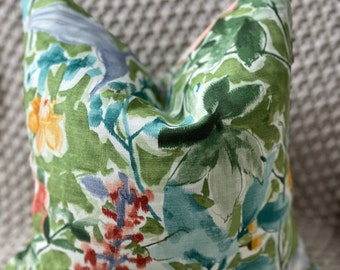 May include: A green throw pillow with a floral pattern featuring blue, red, and yellow flowers. The pillow has a white background and is made of a soft, textured fabric.