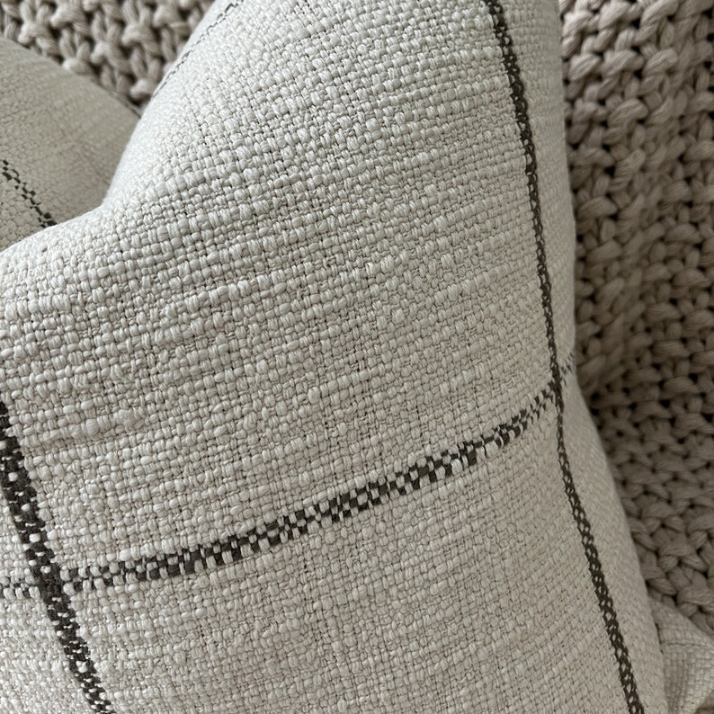 May include: A close-up of a cream-colored throw pillow with a subtle black and white checkered pattern. The pillow is made of a textured fabric and has a soft, cozy feel.