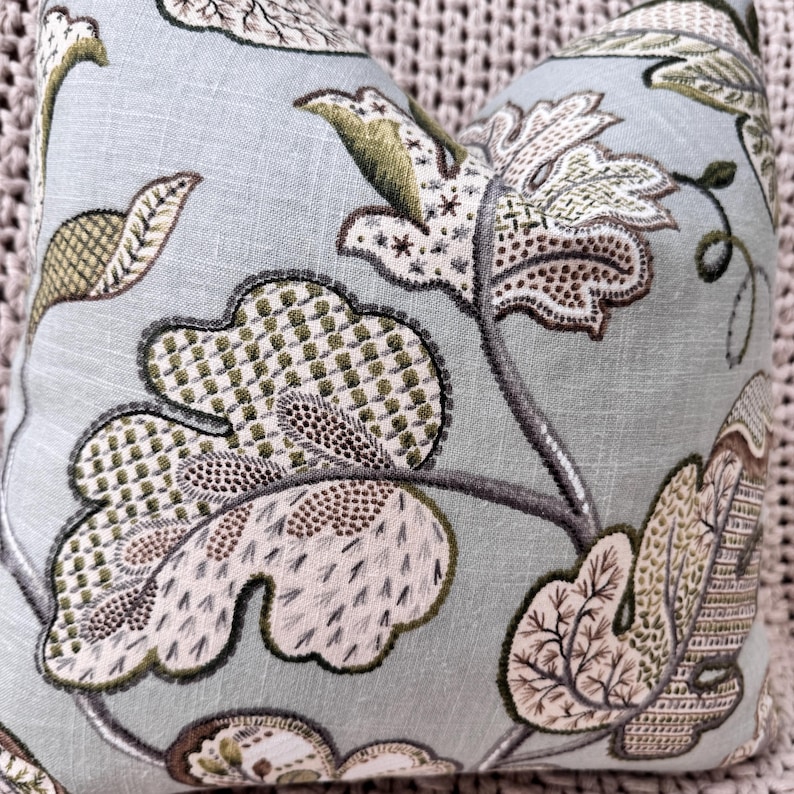 Peut inclure: Un coussin bleu clair avec un motif floral dans les tons de brun, vert et blanc. Le coussin pr&eacute;sente un motif floral stylis&eacute; avec des d&eacute;tails complexes.