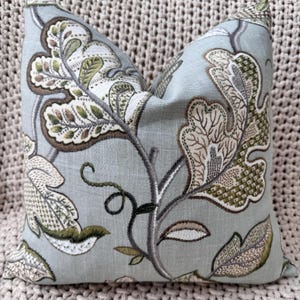 Peut inclure: Un coussin bleu clair avec un motif floral brod&eacute; dans des tons de vert, marron et beige. Le coussin pr&eacute;sente un motif feuillu avec des d&eacute;tails complexes.