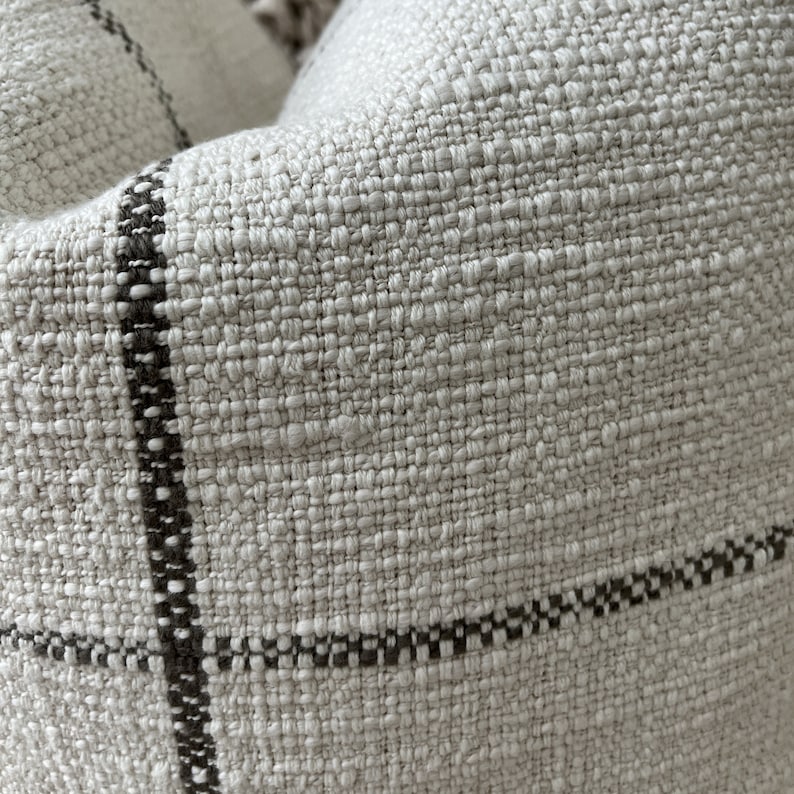 May include: Close-up of a cream-colored woven fabric with black stripes. The fabric has a textured, slightly rough surface.