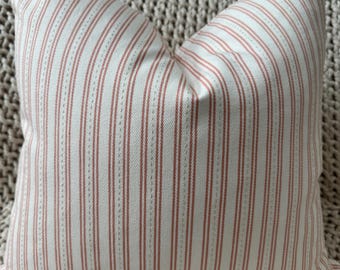 May include: A square pillow with a white background and vertical stripes in a muted red color. The pillow has a classic ticking stripe pattern, with thin, evenly spaced stripes. The fabric appears to be a soft cotton or linen.