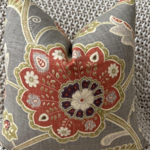 May include: A gray throw pillow with a floral pattern in shades of red, green, and white. The pillow has a textured fabric and a subtle sheen.