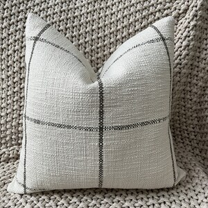 May include: A white throw pillow with a black and white plaid pattern. The pillow is made of a soft, textured fabric.