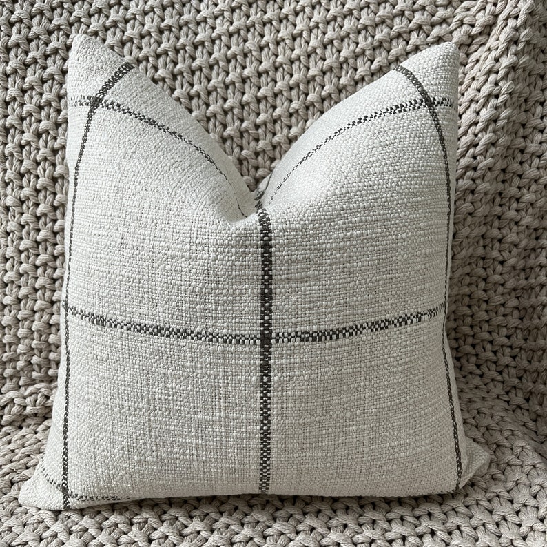 May include: A white throw pillow with a black and white plaid pattern. The pillow is made of a soft, textured fabric.