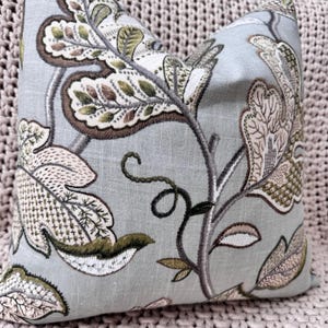 Peut inclure: Un coussin bleu clair avec un motif floral brod&eacute; dans des tons de vert, marron et rose. Le coussin pr&eacute;sente un motif r&eacute;p&eacute;titif de feuilles et de fleurs.