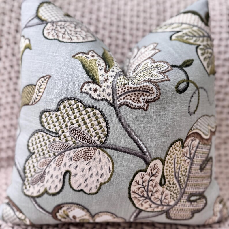 Peut inclure: Un coussin bleu clair avec un motif floral dans les tons de vert, marron et blanc. Le coussin pr&eacute;sente un design d&eacute;licat et complexe avec une esth&eacute;tique vintage.