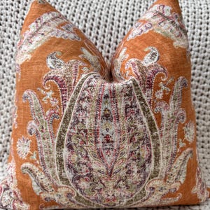 May include: A decorative throw pillow with a paisley pattern in shades of orange, brown, green, and white. The pillow is made of a soft, textured fabric.