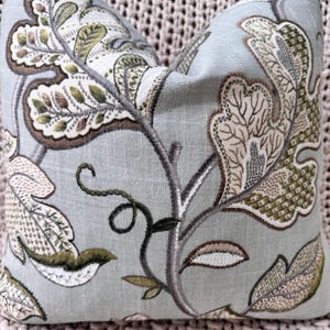 Peut inclure: Un coussin bleu clair avec un motif floral dans les tons de brun, vert et blanc. Le coussin pr&eacute;sente un motif r&eacute;p&eacute;titif de feuilles et de vignes.