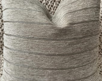 Peut inclure: Un coussin décoratif gris avec des rayures horizontales. Les rayures sont d'un gris plus foncé avec une ligne blanche pointillée au-dessus et en dessous de chaque rayure. Le coussin est en tissu doux et texturé.