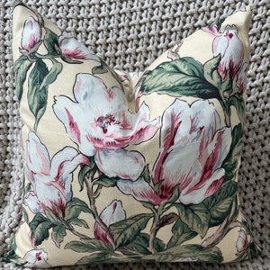 May include: A cream-colored pillow with a floral pattern featuring pink and white magnolia blossoms and green leaves.