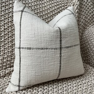 May include: A white throw pillow with a black and white checkered pattern. The pillow is made of a soft, textured fabric.