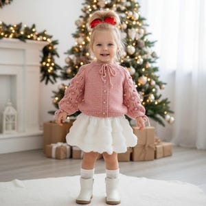 Casaquinho de bebê tricotado à mão, suéter rosa com mangas bufantes.