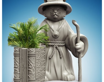 May include: A gray cat statue wearing a robe and a hat, holding a staff. The statue is standing next to a gray planter shaped like a book, with a green plant growing inside.